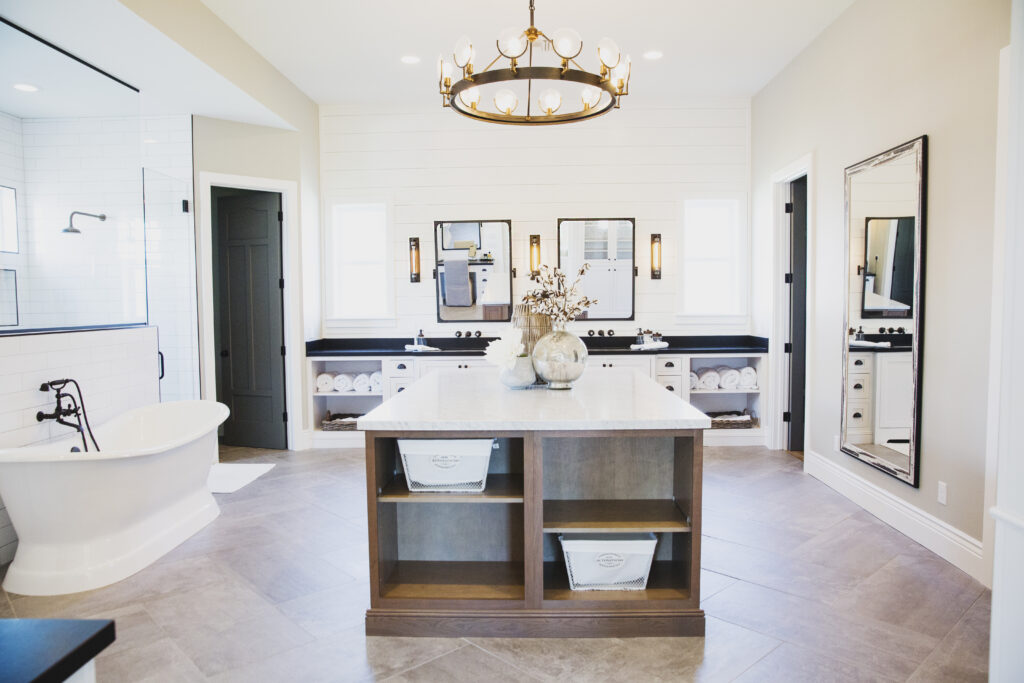 Primary bathroom with a central marble-top vanity island, freestanding tub and brass chandelier