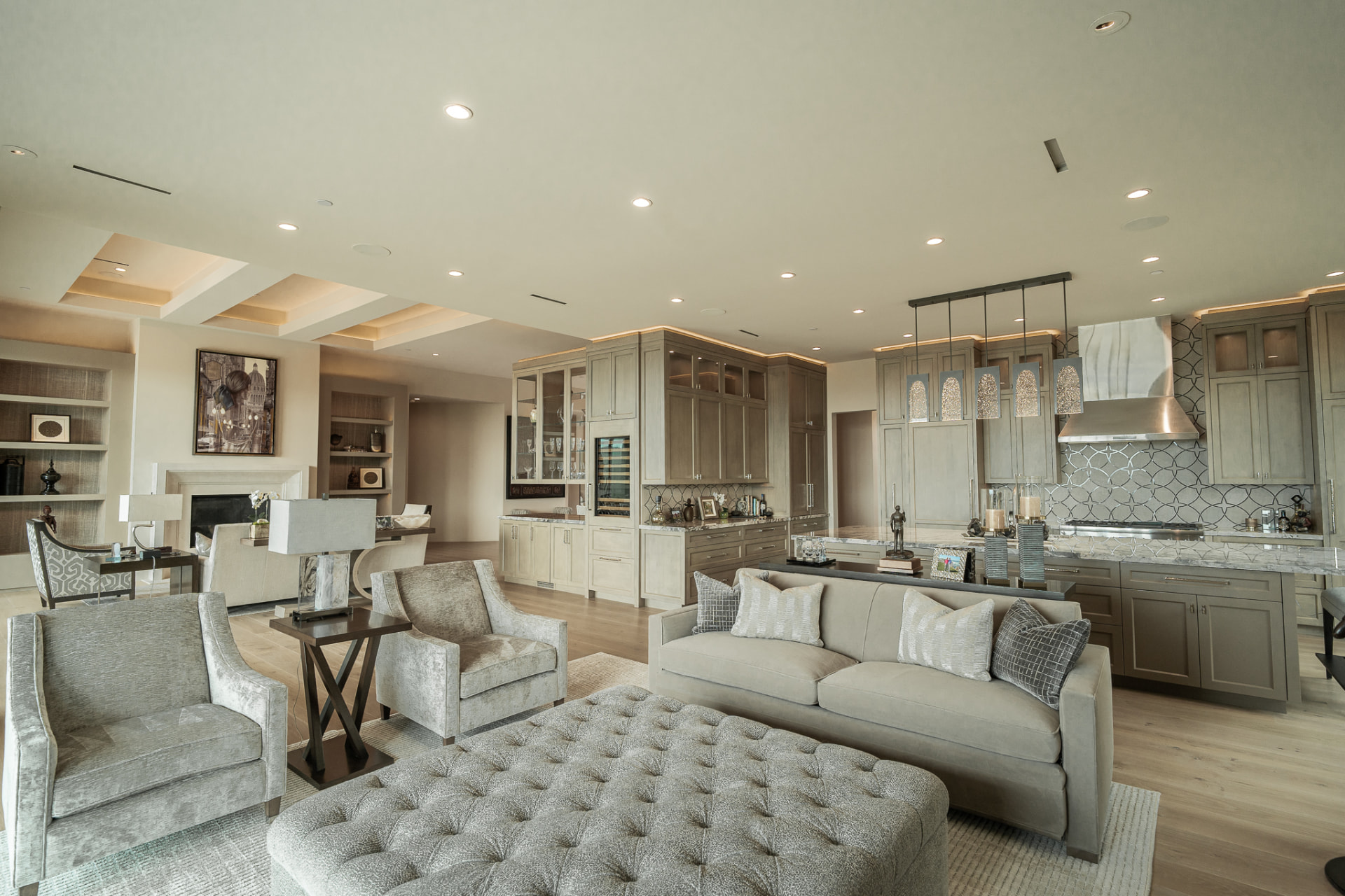 Open great room with a tufted ottoman, sofa and accent chairs, with the kitchen island and bar beyond
