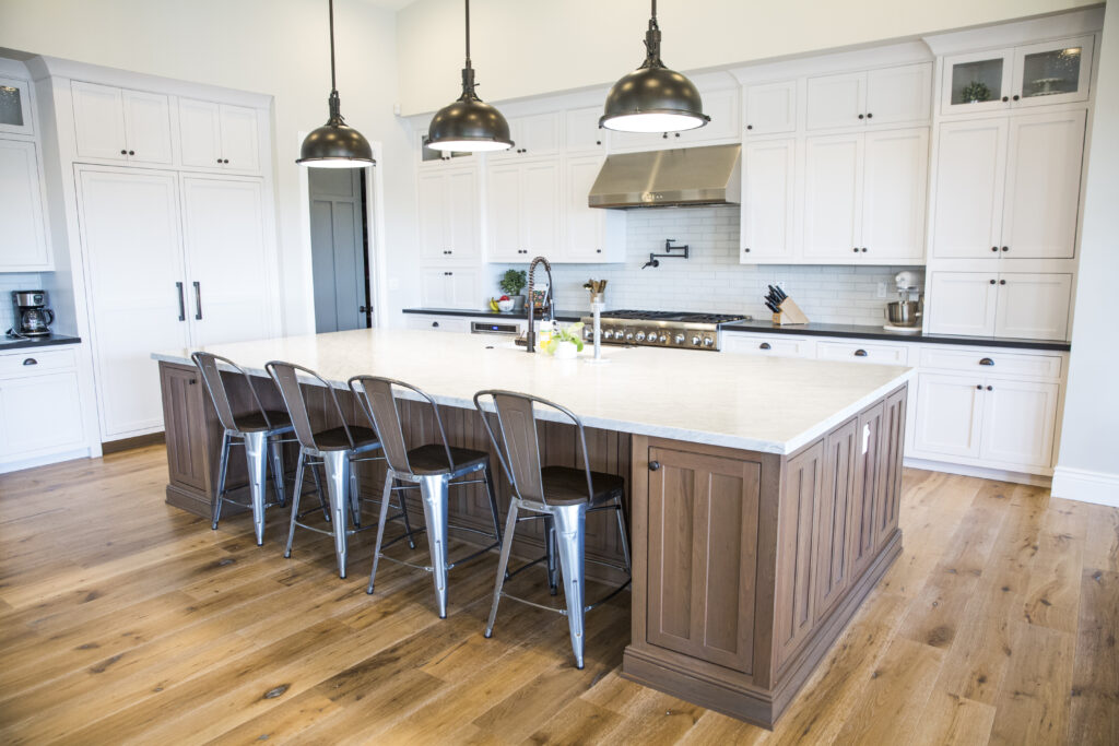 Kitchen with white cabinetry, walnut island with bar stools and stainless-steel pendants
