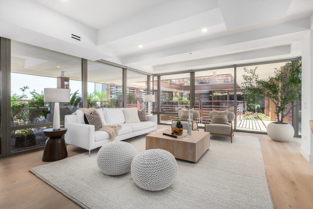 Living room with a white sofa, wood coffee table and an olive tree beside glass walls