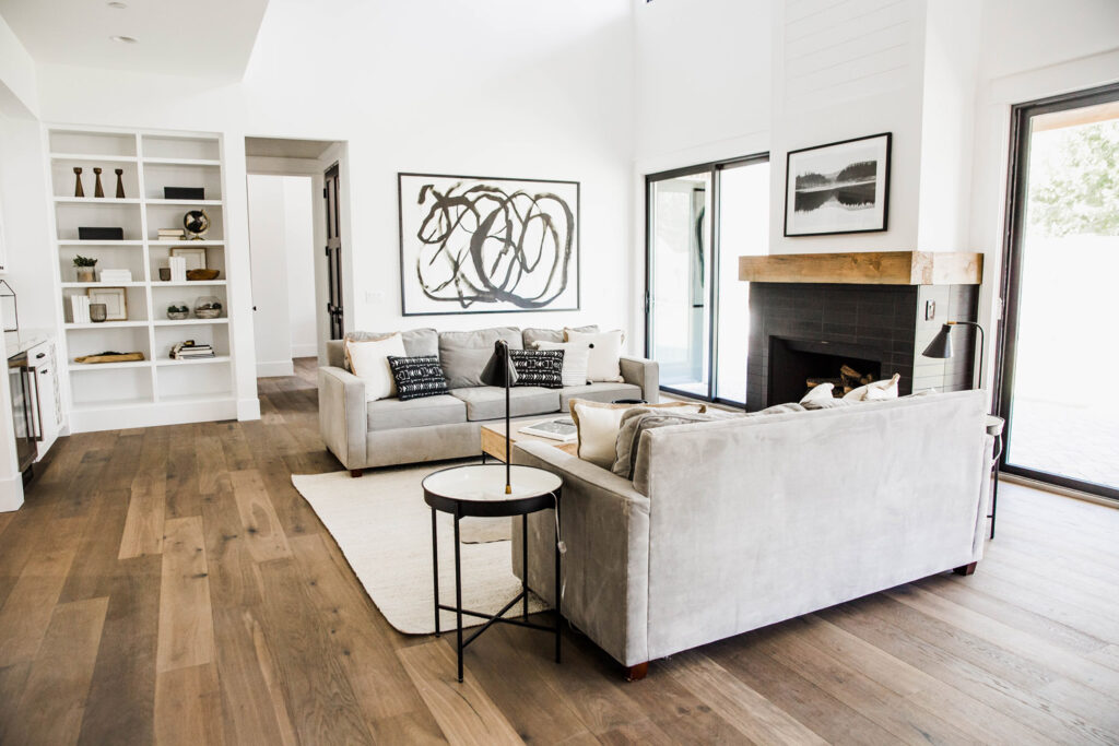 Living room with two grey sofas, built-in white shelving, a black tiled fireplace with a wood mantel and sliding glass doors opening to the patio