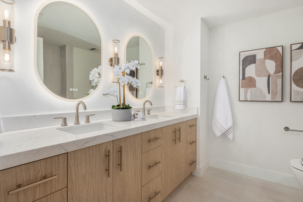 Bathroom with a double-sink oak vanity, backlit oval mirrors and quartz countertop