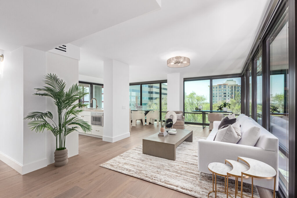 Open-plan living room with floor-to-ceiling windows, a white sofa and views of mature trees