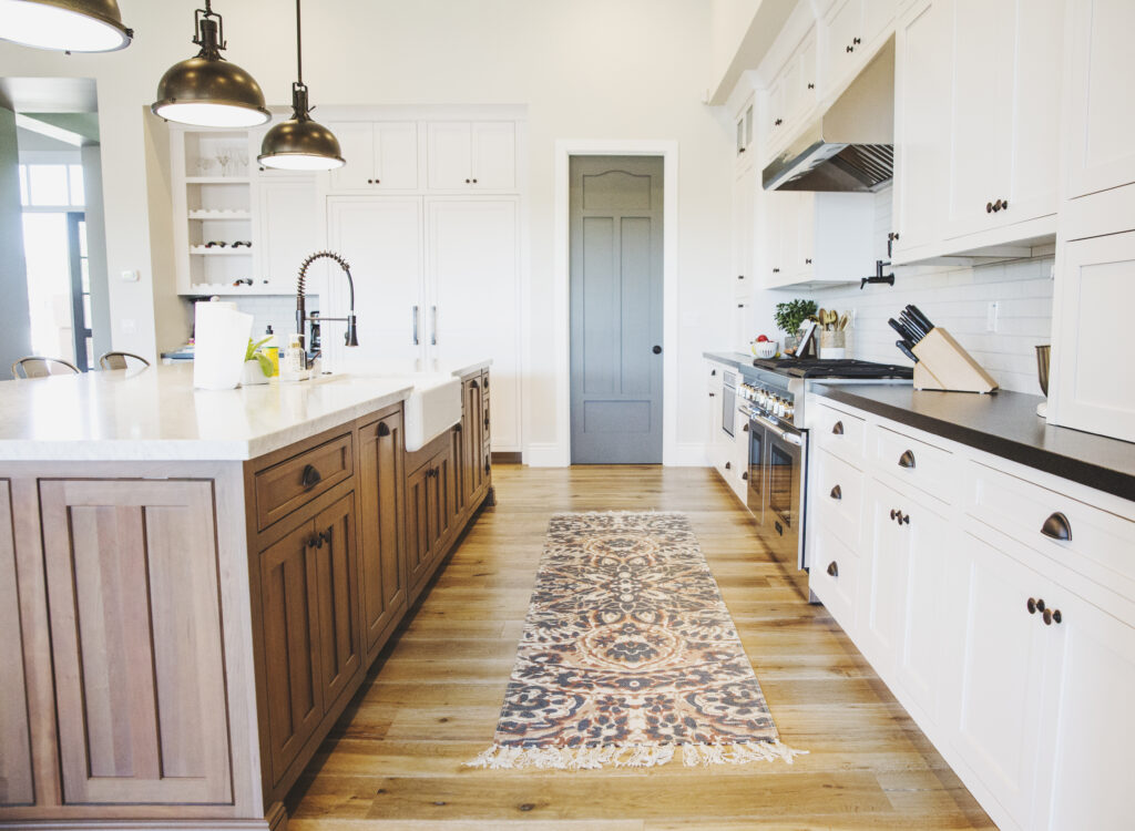 Kitchen with a two-tone island, farmhouse sink, stainless range and a runner rug on oak floors