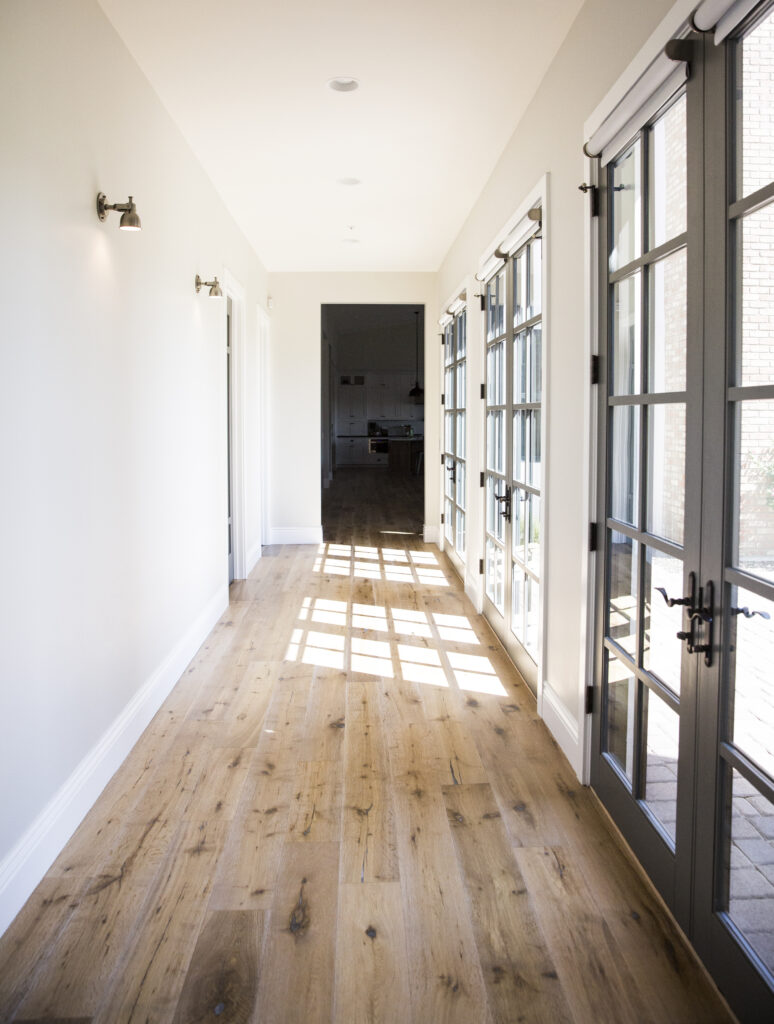 Hallway with wide-plank oak floors and glass-paneled French doors opening to the patio
