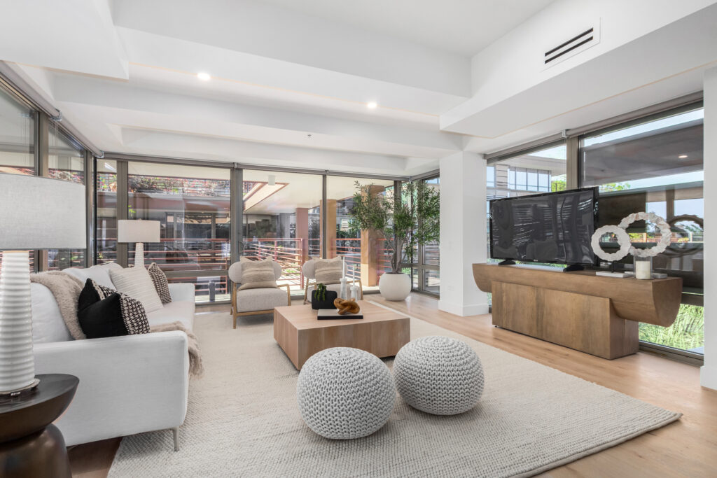 Living room with a white sofa, woven poufs and floor-to-ceiling windows opening to a landscaped courtyard