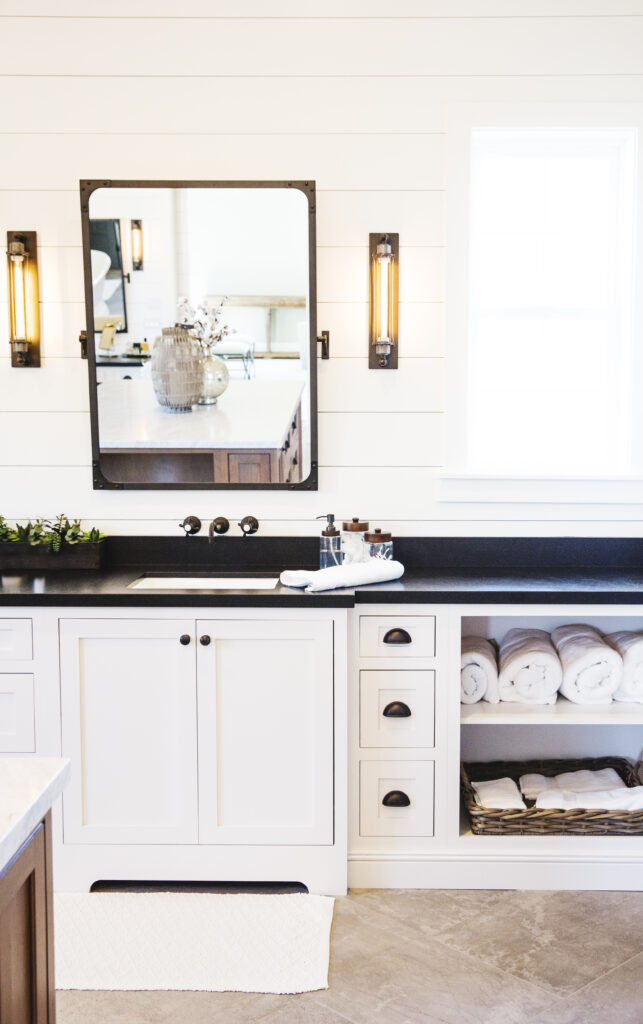 Bathroom vanity with black countertop, industrial sconces and a framed pivot mirror