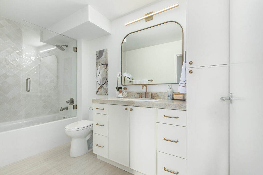 Bathroom with a single-sink vanity, a brass-framed mirror and a glass-enclosed tub and shower